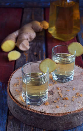 Homemade ginger tincture or ale on wooden background. Rustic style. Spice yellow liqueur in a glass....