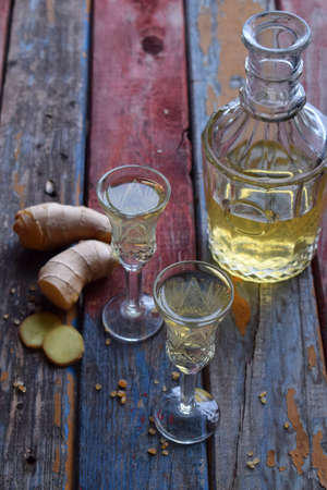 Homemade ginger tincture or ale on wooden background. Rustic style. Spice yellow liqueur in a glass....