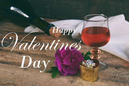 A glass of red wine, bottle and rose on rustic wood table. Valentine's day still life. Concept...