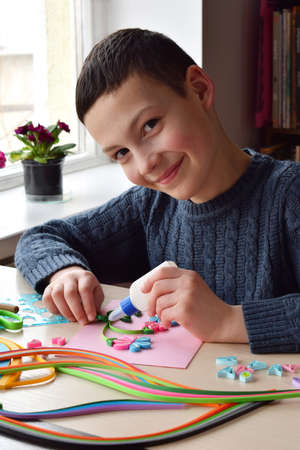 Quilling technique. Boy making decorations or greeting card. Paper strips, flower, scissors. Handmade crafts on holiday: Birthday, Mother's or Father's Day, March 8, Wedding. Children's DIY conceptの写真素材