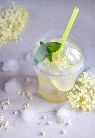 Homemade elderflower lemonade with lemon and elderberry flowers in plastic cup with sphere dome cap and cocktail tube. Elderflower cordial. Summer cold drink.の写真素材