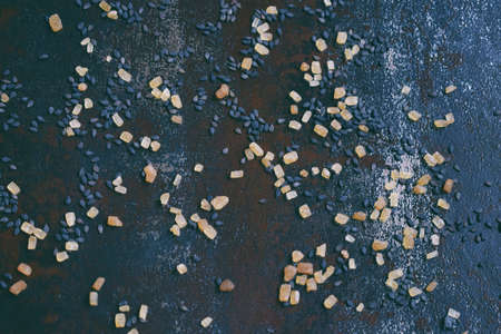 Black sesame seeds and cane sugar on dark concrete background. Food background. Copy space.