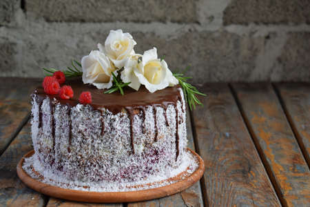 Gluten-free and dairy-free cake decorated with white roses and coconut: chocolate-nut biscuit, berry mousse, custard on almond milk and chocolate glaze. Healthy dietary baking. Vegetarian foodの写真素材