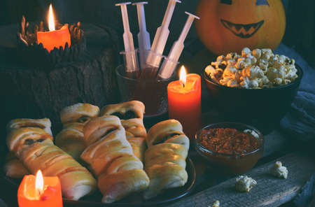 Halloween trick or treat party. Funny delicious food and pumpkin on wooden background - mini pizza, bread sticks, cheese, olives, ketchup, popcorn, juice. Copy space for textの写真素材