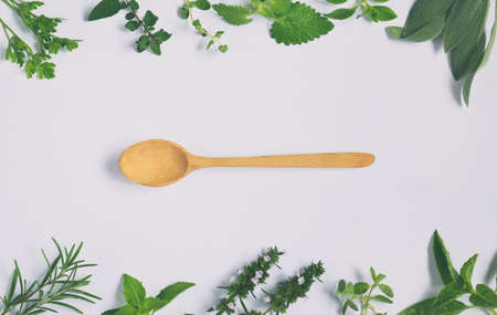 Fresh spicy and medicinal herbs on white background and wooden spoon. Border from various herb - rosemary, oregano, sage, marjoram, basil, thyme, mint. Food frame for recipe.の写真素材