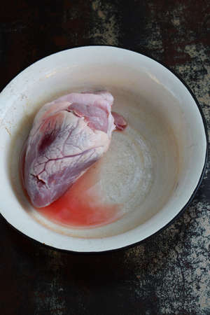 Heart in metal bowl before cooking on black background. Raw meat. Offal.の写真素材