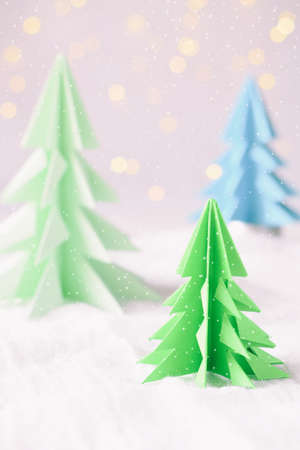 Origami 3D Xmas tree from paper on white background and bokeh lights. Merry Christmas and New Year card. Paper art style. Copy space. Selective focus.の写真素材