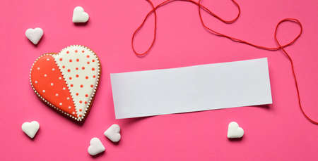 Homemade gingerbread hearts with an empty paper for your text on pink background. Valentine cookies hearts. Edible Valentine's Day Gift or greeting card conceptの写真素材