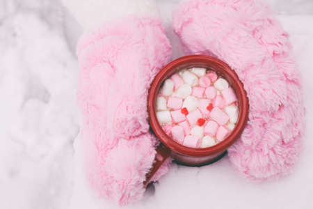 Woman Hands Holding Cup of Hot Chocolate with Marshmallow candies. Fur mittens and Warm cocoa drink. Hello February or Valentines Day concept.の写真素材