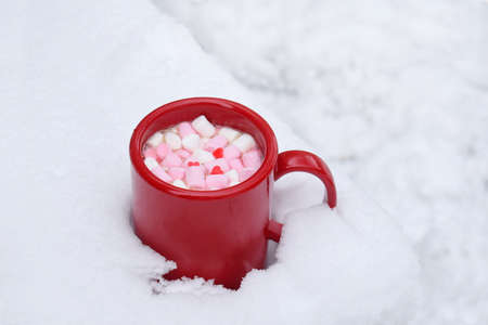 Red Cup of Hot Chocolate with Marshmallow candies in snow. Warm cocoa drink. Hello February or Valentines Day concept.の写真素材