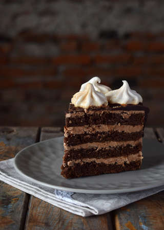 Piece of Chocolate cake decorated with rosettes of meringue cream: chocolate-nut biscuit, caramel...