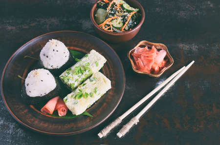 Mix of Japanese food - rice balls onigiri, omelette, pickled ginger, sunomono wakame cucumber salad...