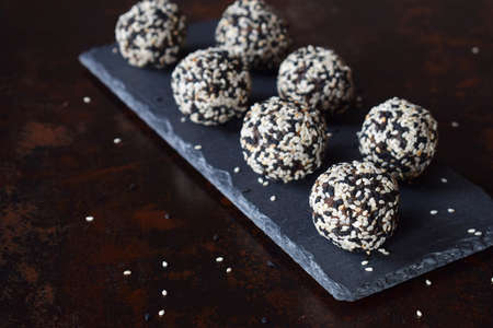 Healthy raw energy bites with flax seeds, almonds, banana and dates. Vegan truffles in sesame seeds on dark background. Homemade candy balls. Raw food. Gluten free. Dairy freeの写真素材