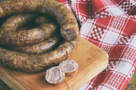 The traditional smoked sausage ring in a rustic style. Appetizing sausages made of pork and lamb with fresh herbs, spices on the wooden board. Free space for text.の写真素材