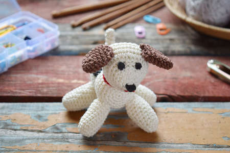 Making crochet white dog. The toy for babies or trinket. On the table threads, needles, hook, cotton yarn. Handmade gift. DIY crafts concept.の写真素材