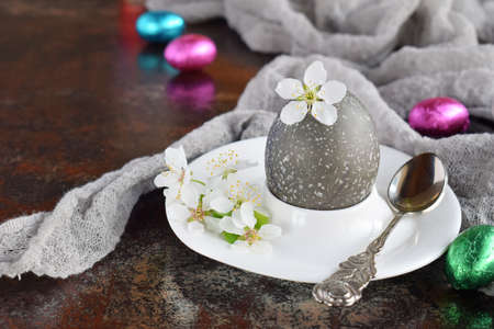 Black colored egg and flowers on clay plate. happy easter card. Holidays breakfast concept. Festive...