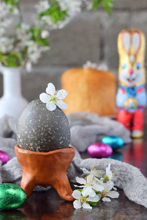Black colored eggs and flowers on clay plate. Happy Easter card. Holidays breakfast concept. Festive table place setting decoration with blossom, bunny, chocolate eggs.の写真素材