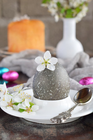 Black colored eggs and flowers on clay plate. Happy Easter card. Holidays breakfast concept. Festive table place setting decoration with blossom, bunny, chocolate eggs.の写真素材