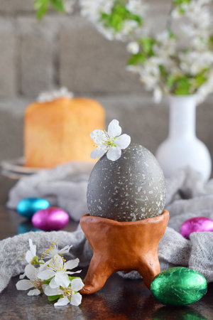 Black colored eggs and flowers on clay plate. Happy Easter card. Holidays breakfast concept. Festive table place setting decoration with blossom, bunny, chocolate eggs.の写真素材