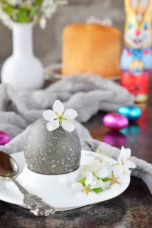 Black colored eggs and flowers on clay plate. Happy Easter card. Holidays breakfast concept. Festive table place setting decoration with blossom, bunny, chocolate eggs.の写真素材