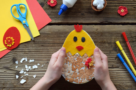Making of handmade Easter decoration. Child made greeting card from eggshell. Childrens DIY concept, gift with your own hands. Hobby, paper crafts at home or in kindergarten.の写真素材