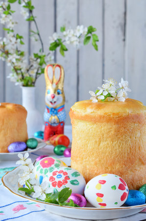 Happy Easter concept. Sweet bread with dried fruits and colored eggs. Holidays breakfast. Orthodox kulich. Festive table place setting decoration with paska, blossom twigs, bunny, chocolate egg.の写真素材