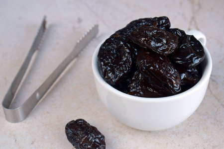 Dried Prunes in White Bowl on Neutral Background. Healthy Snack for Vegan Diet, Rich in Fiber and Nutrients, Ideal for Culinary Recipes, Desserts, and Weight Managementの写真素材