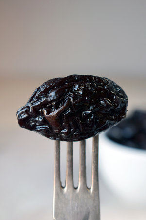 Close-Up of Fork Holding Soft Dried Prune Over a Bowl. Delicious Natural Food Ingredient for Cooking, Baking, and Nutritious Eating with Sweet and Juicy Textureの写真素材