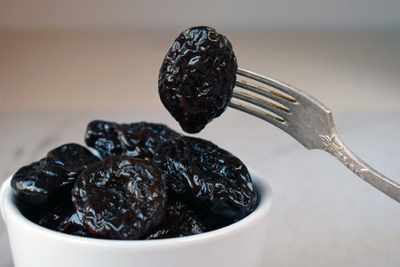 Tasty Dried Plums in Ceramic Dish on Kitchen Table. Dark Wrinkled Fruit for Healthy Lifestyle, Boosting Digestion, and Energy with Natural Sweetnessの写真素材