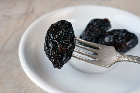Tasty Dried Plums in Ceramic Dish on Kitchen Table. Dark Wrinkled Fruit for Healthy Lifestyle, Boosting Digestion, and Energy with Natural Sweetnessの写真素材