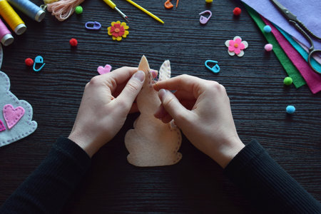 Sewing felt bunny ornament by hand, Easter DIY decoration, needlework process, creative festive project, spring holiday craft, colorful workspace, threads, buttons, handmade preparationの写真素材