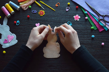 Stitching felt bunny ornament, Easter handmade DIY project, festive creative process, holiday decoration crafting, colorful materials, workspace, threads, buttons, spring celebration preparationの写真素材