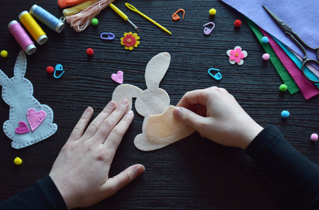 Holding felt bunny ornament, Easter DIY decoration, handmade crafting project, festive preparation, creative process, colorful materials, threads, scissors, spring holiday accessory workspaceの写真素材