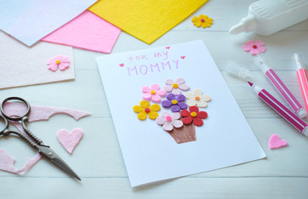 Handmade Mothers Day Greeting Card Creation. DIY Craft Project with Felt Flowers, Colorful Paper, and Scissors on White Wooden Background. Creative Holiday Gift Idea for Mom, Festive Cardmaking Process with Crafting Suppliesの写真素材