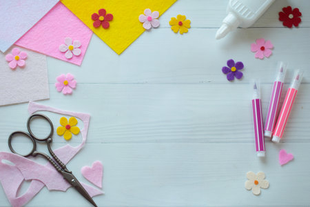 Flat lay composition of DIY greeting card crafting materials, including colorful felt flowers, scissors, glue, arranged on a white wooden background, showing the process of creating a personalized handmade card for special occasionsの写真素材