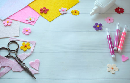 Flat lay composition of DIY greeting card crafting materials, including colorful felt flowers, scissors, glue, arranged on a white wooden background, showing the process of creating a personalized handmade card for special occasionsの写真素材