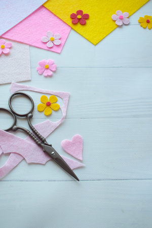 Flat lay composition of DIY greeting card crafting materials, including colorful felt flowers, scissors, glue, arranged on a white wooden background, showing the process of creating a personalized handmade card for special occasionsの写真素材