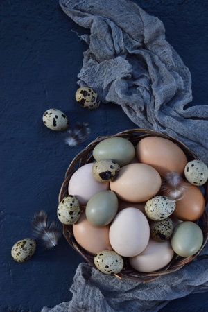 Rustic still life with colorful chicken and quail eggs placed on a dark fabric background perfect for farm-fresh organic food concepts Easter decorations and countryside lifestyle themesの写真素材