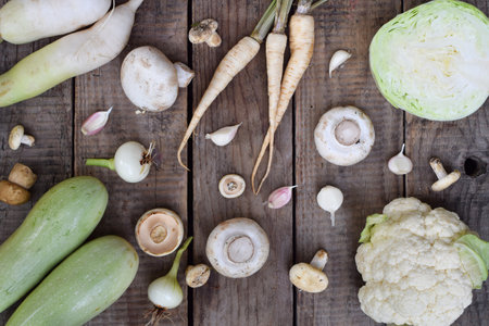 Top view of assorted white vegetables including zucchini mushrooms and cauliflower on a rustic wooden table perfect for vegetarian recipes organic farming concepts and healthy food promotionsの写真素材