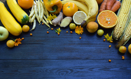 Arrangement of yellow fruits and vegetables on a blue rustic background featuring apples lemons corn and beans ideal for healthy food promotions vegetarian concepts and colorful kitchen visualsの写真素材