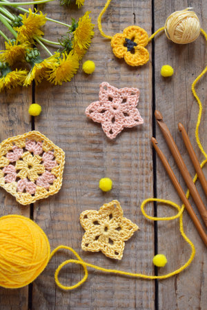 Rustic flat lay of yellow crochet flowers yarn balls and dandelions on wooden table perfect for spring DIY crafting projects and handmade decor conceptsの写真素材