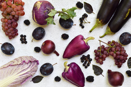 Flat lay of purple and black fruits and vegetables on a white background featuring grapes plums and eggplants perfect for healthy food promotions vegetarian recipes and colorful kitchen designsの写真素材