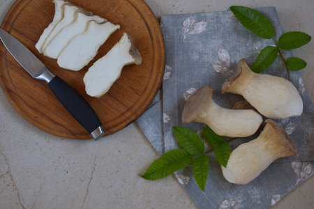 Sliced king oyster mushrooms arranged on a rustic wooden plate with knife and green onions. Perfect for vegetarian cooking projects, farm-to-table food visuals, and organic kitchen scenes.の写真素材
