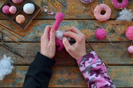 Hands shaping neck of pink amigurumi dinosaur using crochet hook wool yarn and stuffing during...
