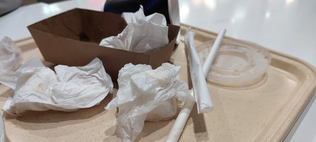 Paper napkins plastic cutlery and fast food box left on tray after quick meal disposable waste pollution problem in self service cafeteria trash accumulation eating habits conceptの写真素材