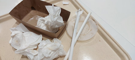 Used paper napkins disposable tableware cardboard box plastic straws dirty food tray in food court...