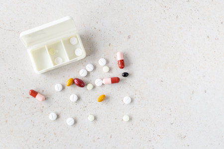 Set of colorful medical pills, capsules and vitamins near weekly pill organizer on light background....