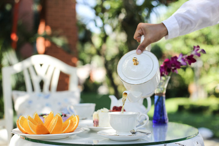 Afternoon tea with a man pouring tea from pot in to a cupの写真素材