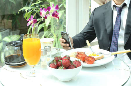 Businessman using mobile phone working while having a breakfastの写真素材