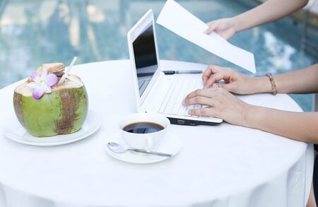 Woman working with laptop computer sitting at swimming pool and drinkの写真素材